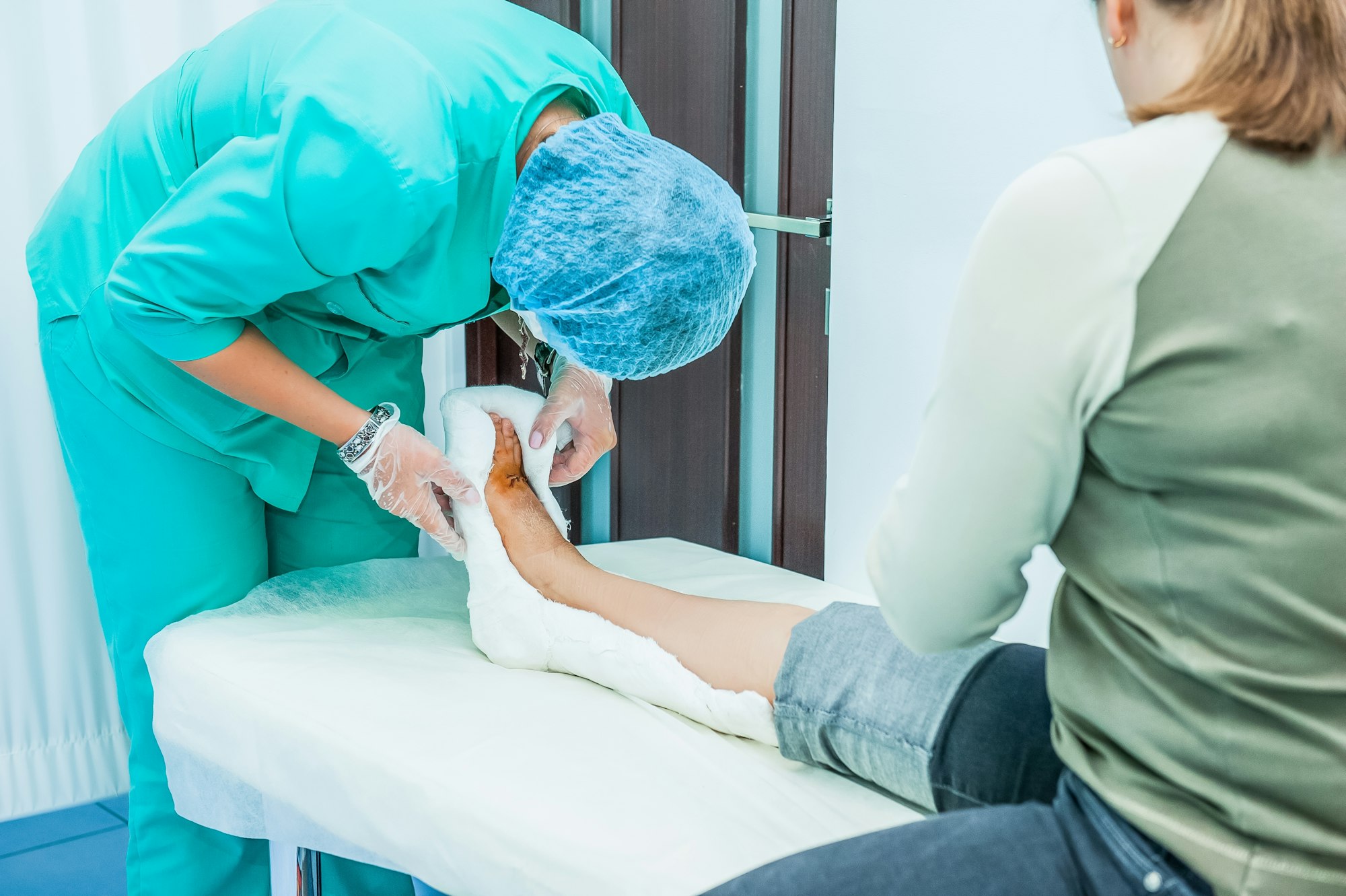 The doctor treats the wound on the patient's leg in a clinic room.